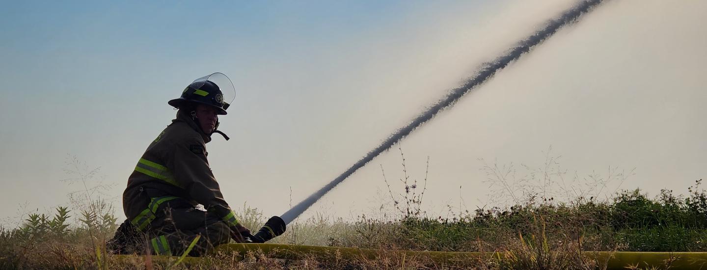 Firefighter holding hose spraying water into field