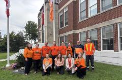 staff wearing orange shirts standing in front of lowered flags